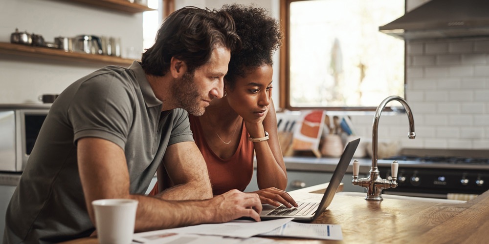 Couple hunched over a laptop on the kitchen counter