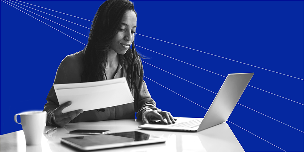 Woman holding papers while working on a laptop