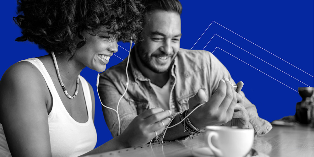 Man and woman sharing headphones while looking at phone