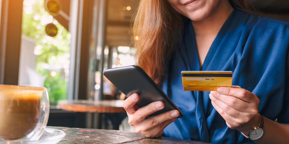 Woman holding credit card in one hand and phone in her other hand