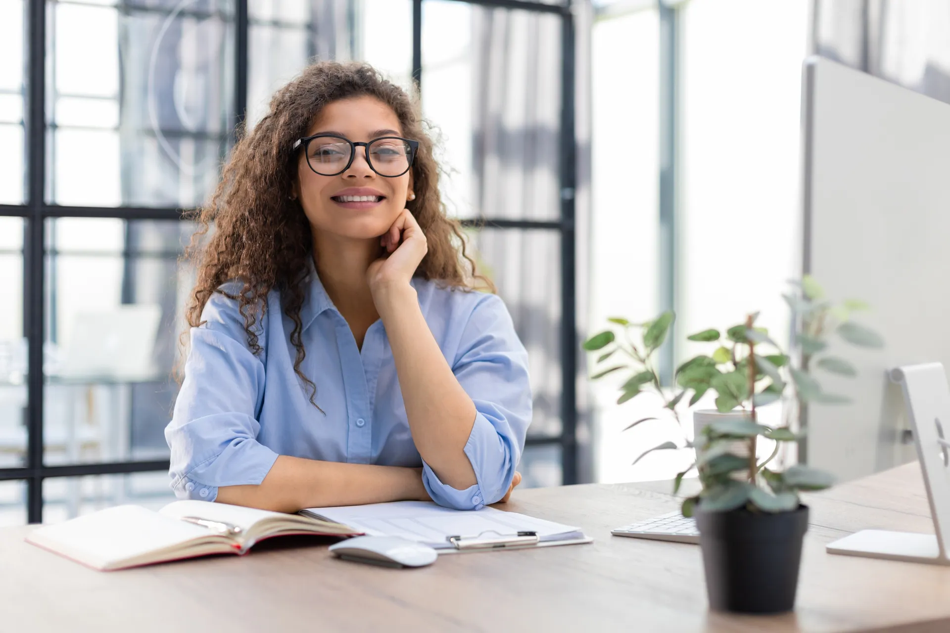 Young woman with glasses sitting at a desk with a plant