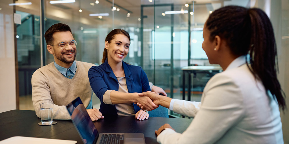 Young couple smiling and shaking hands with an advisor in an office