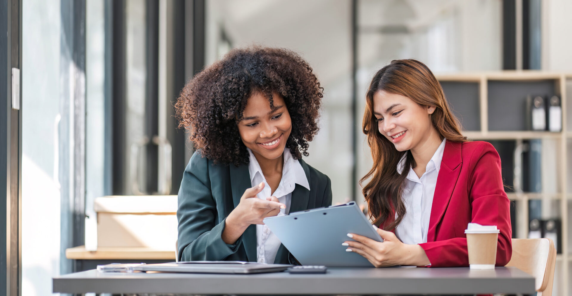 Two professional woman reviewing paperwork over coffee