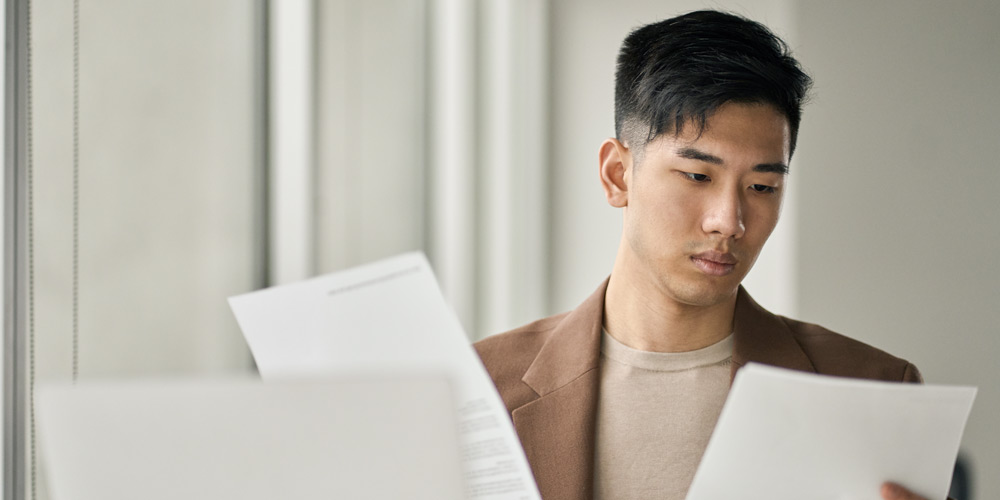 Man in a brown sport coat looking intently at two pieces of paper