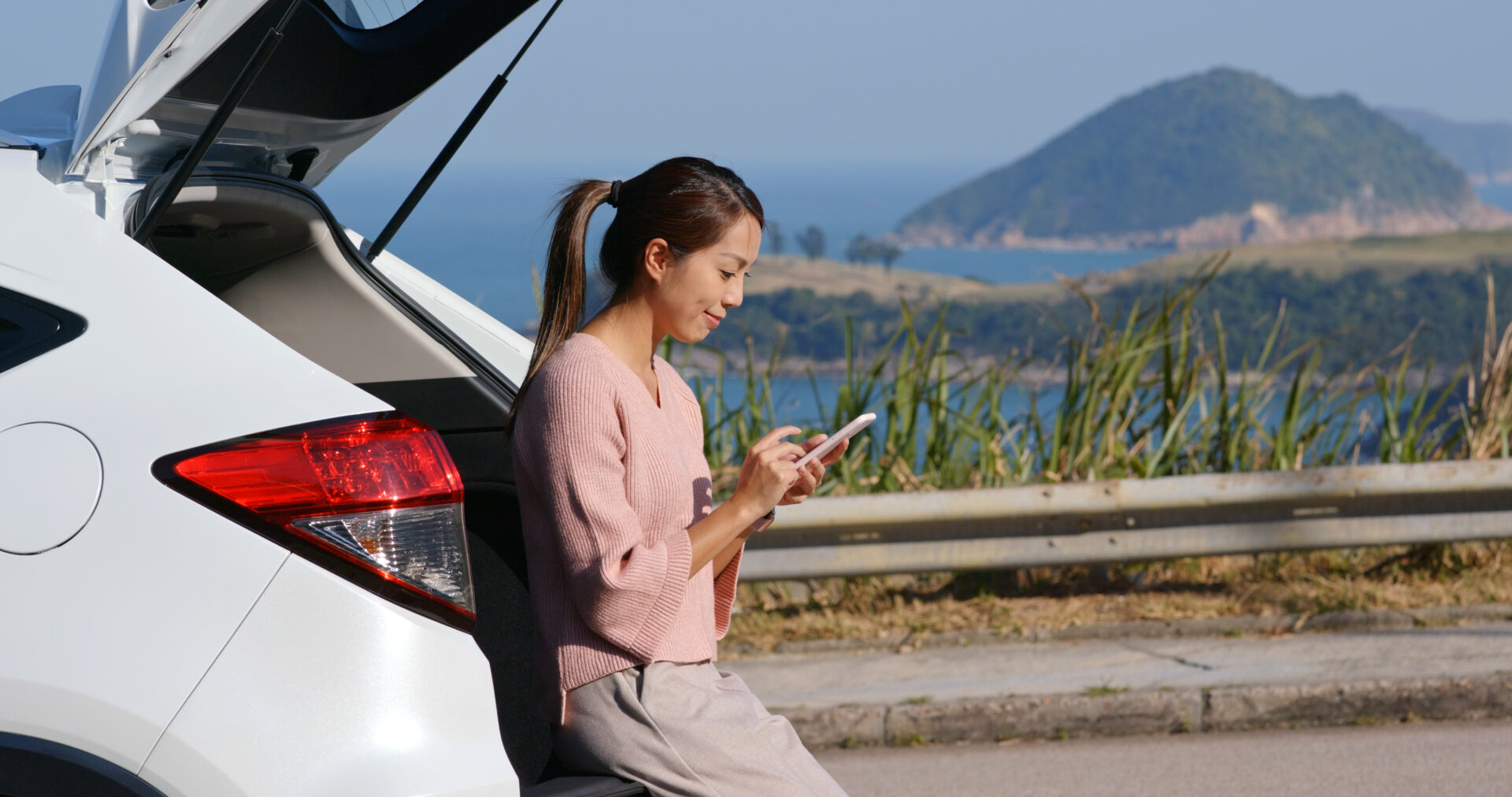Woman sitting in the hatchback of her car typing on her phone