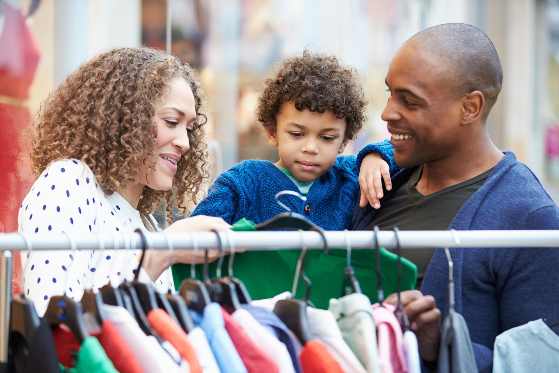 husband, wife, and son looking at clothes on a rack