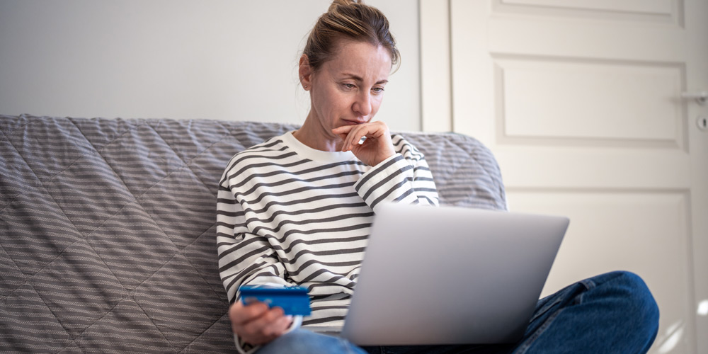 Woman in striped shirt holding a credit card and looking at laptop screen